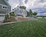 Wide view of a waterfront backyard with a custom in-ground pool and stone patio in Long Lake